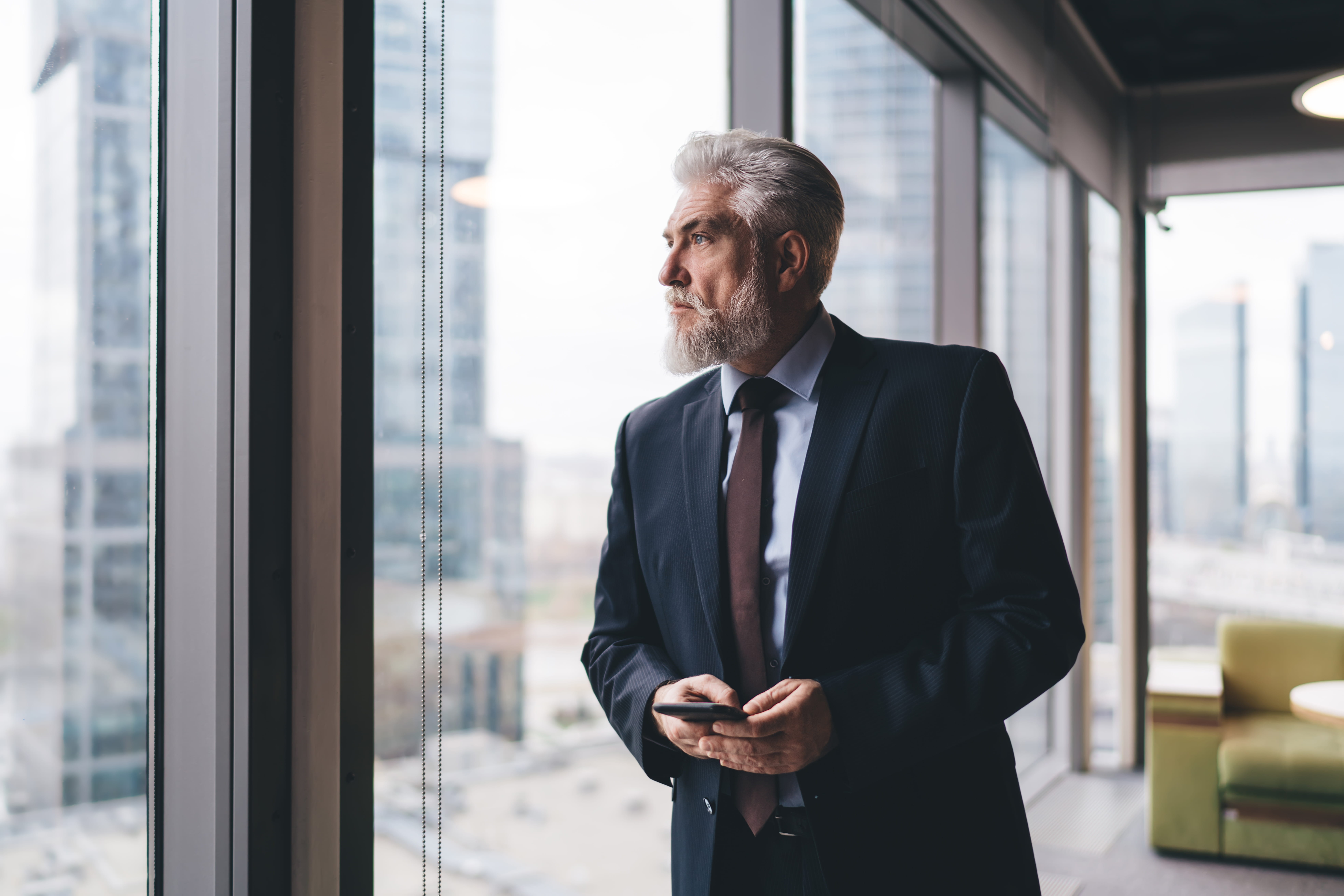 Man in suit looking pensive staring out of window while considering business succession planning